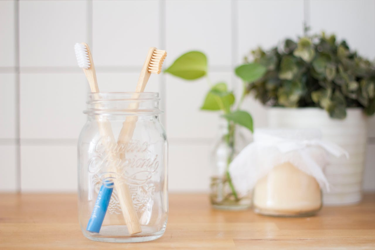 Eco-friendly bamboo toothbrushes in a glass jar with potted plants on a wooden surface.