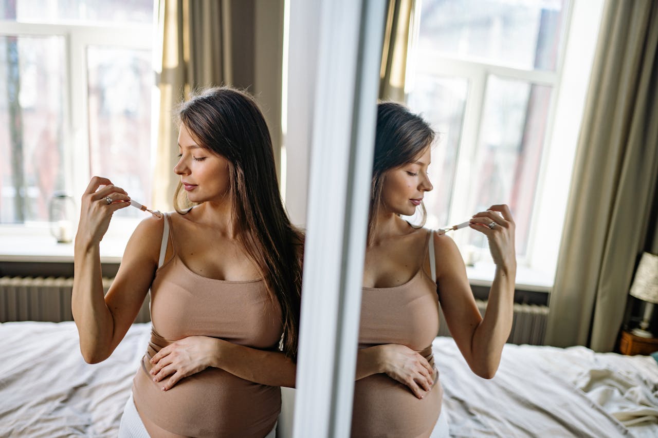 Pregnant woman practicing self-care with jade roller in a serene bedroom setting.